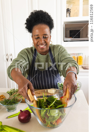 Happy senior african american woman making salad in kitchen at home Happy senior african american woman making salad in kitchen at home 116812569