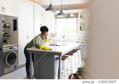 Happy senior african american woman wiping table in kitchen at home 116812607
