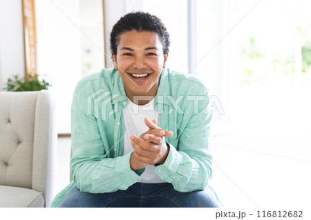 Young biracial man smiles warmly during a video call in a bright home setting 116812682