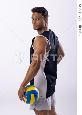 Young biracial man poses confidently in sportswear, holding a volleyball on a white background Young biracial man poses confidently in sportswear, holding a volleyball on a white background 116812839