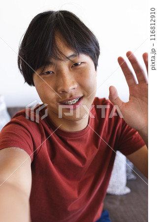 Asian college student waving at camera, sitting indoors Asian college student waving at camera, sitting indoors 116812910
