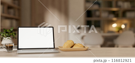 A laptop computer with a white-screen mockup on a wooden table in a contemporary apartment. 116812921