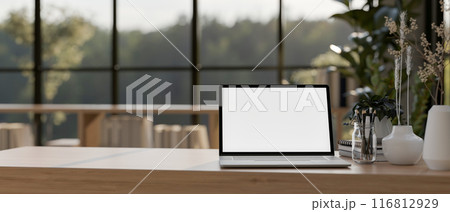 A laptop computer with a white-screen mockup on a wooden table in a contemporary room. 116812929