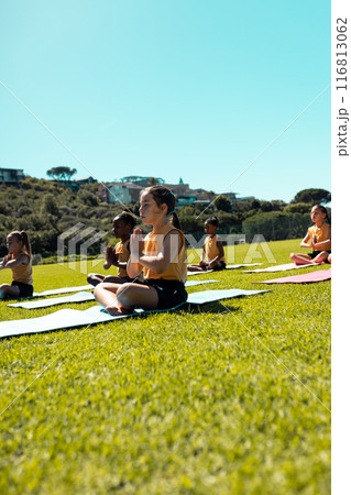 Diverse schoolgirls meditate in prayer pose on grass, clear sky above Diverse schoolgirls meditate in prayer pose on grass, clear sky above 116813062