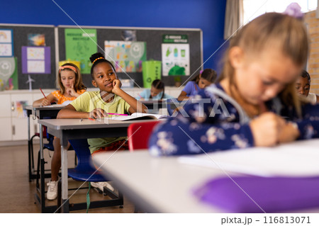African american schoolgirl thinking while studying with children in classroom 116813071