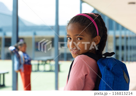 A young African American girl with blue backpack smiles, copy space 116813214