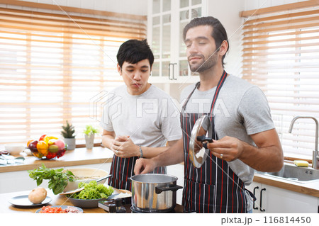 LGBTQ+ gay bisexual cooking their meal together in the kitchen, LGBTQ gay couple making a spaghetti. A different ethnicity handsome gay couple enjoy cooking a spaghetti together in kitchen. 116814450