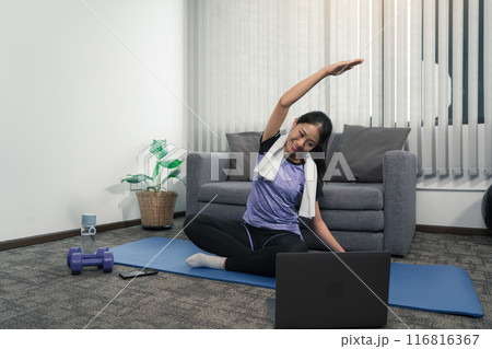 Asian woman stretching during a yoga class with a trainer at her laptop computer at home. Asian woman stretching during a yoga class with a trainer at her laptop computer at home. 116816367