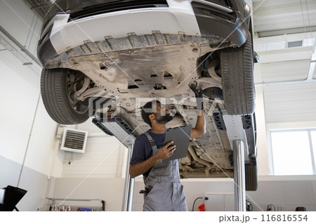 Auto mechanic inspecting car on hydraulic lift in garage Auto mechanic inspecting car on hydraulic lift in garage 116816554