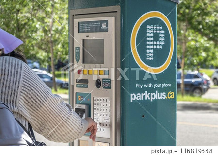 Calgary, Alberta, Canada. Jul 07, 2024. A person uses a Calgary Parking Authority parking meter to pay for parking. The meter has a digital display and accepts coins or mobile payment via ParkPlus 116819338