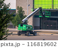 Calgary, Alberta, Canada. Jul 20, 2024. A green telescopic boom lift is positioned in front of a commercial building, with its platform elevated for maintenance work. 116819602