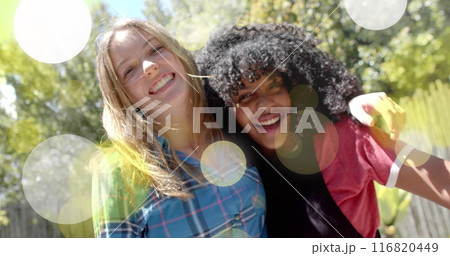 Image of yellow and white light spots over two happy diverse teenage girls embracing in garden Image of yellow and white light spots over two happy diverse teenage girls embracing in garden 116820449