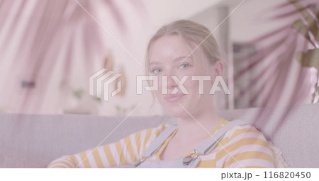 Image of palm leaves over smiling caucasian teenage girl relaxing at home 116820450