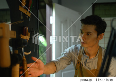 Asian male artisan working with leather, using a various of tools in the workshop Asian male artisan working with leather, using a various of tools in the workshop 116821046