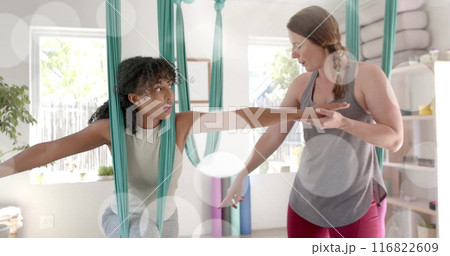 Image of light spots over diverse female instructor and teenage girl practicing aerial yoga Image of light spots over diverse female instructor and teenage girl practicing aerial yoga 116822609