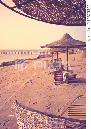 A tranquil beach with sun loungers and umbrellas at sunset, color toning applied, Marsa Alam region, Egypt. 116823596