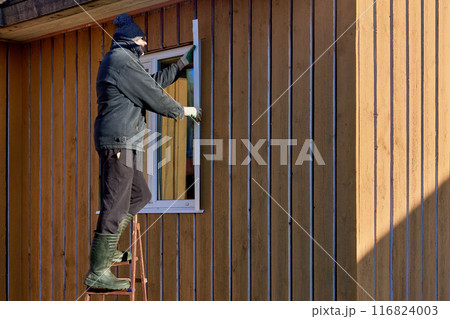 Standing on stepladder, roofing contractor installs metal window slopes on facade side. 116824003