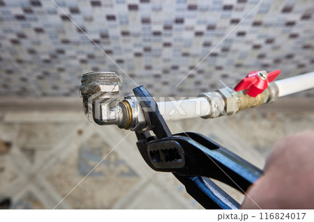 Plumber uses an adjustable wrench to loosen nut of compression fitting in domestic plumbing system. 116824017
