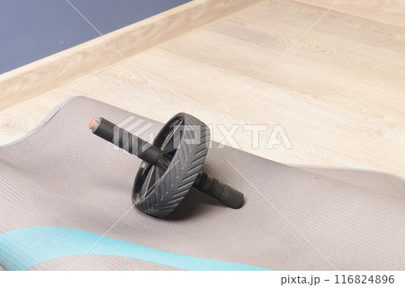 Fitness gymnastic wheel with two handles on mat in room. Equipment for sports activities. Health and movement.  116824896