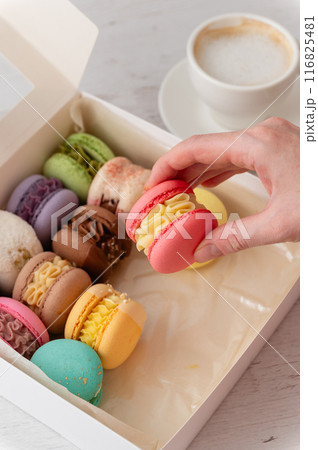 A woman's hand takes out a delicious macaroon from a box. A woman's hand takes out a delicious macaroon from a box. 116825481