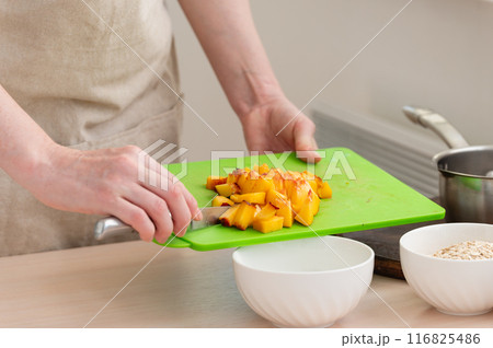 A woman adds chopped peach to her oatmeal. 116825486
