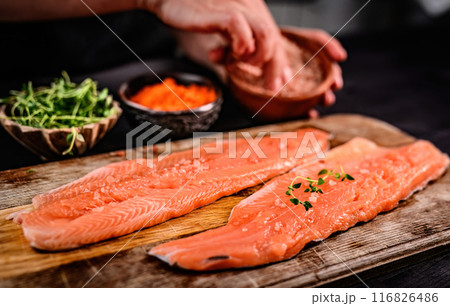 Fresh trout salmon filet with herbs greens on wooden board and chief hands on blurred background. Omega orange fish with rosemary for healthy nutrition 116826486