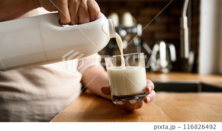 Pouring milk in glass at kitchen at home Pouring milk in glass at kitchen at home 116826492