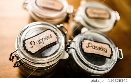 Set of different spicies in glass jars at the kitchen. Black pepper and dried greens. Set of different spicies in glass jars at the kitchen. Black pepper and dried greens. 116826542