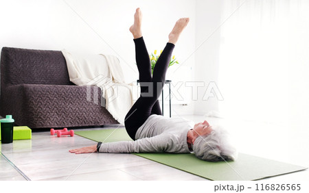 Elderly Woman With Grey Hair At Home Doing Yoga And Stretching Exercises, Looking Attractive 116826565