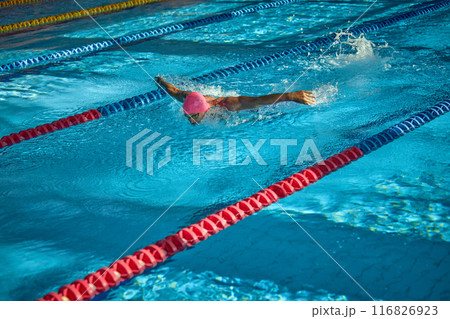 Side view of swimmer glides powerfully through water with butterfly stroke, his focused expression and strong arms making splash in clear blue lane. Side view of swimmer glides powerfully through water with butterfly stroke, his focused expression and strong arms making splash in clear blue lane. 116826923