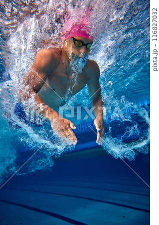 Underwater shot of dedicated swimmer in training, wearing pink cap and goggles, showcasing his toned physique and powerful stroke. Underwater shot of dedicated swimmer in training, wearing pink cap and goggles, showcasing his toned physique and powerful stroke. 116827032