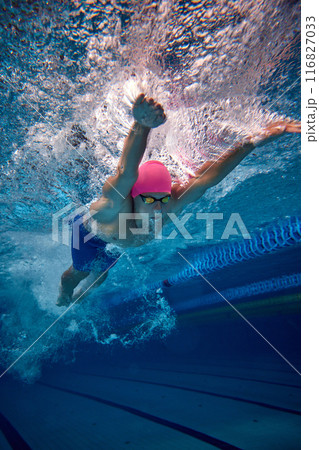 Male swimmer, highlighting his efficient freestyle technique, wearing blue trunks and goggles in pool underwater. 116827033
