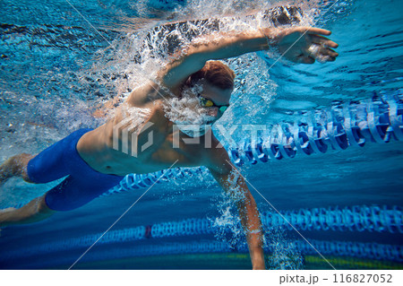 Male swimmer captured mid-stroke underwater, showcasing his strength and technique, as he glides through pool, wearing blue swimwear and goggles, Male swimmer captured mid-stroke underwater, showcasing his strength and technique, as he glides through pool, wearing blue swimwear and goggles, 116827052