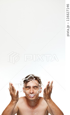 Poster. Young man washing, splashes water on his face against white studio background in modern bathroom. Refreshing skincare routine Poster. Young man washing, splashes water on his face against white studio background in modern bathroom. Refreshing skincare routine 116827146