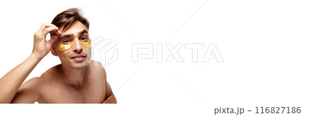 Banner. Young man looks at camera as in mirror and plucks eyebrows with tweezers against white studio background. with copy space. Banner. Young man looks at camera as in mirror and plucks eyebrows with tweezers against white studio background. with copy space. 116827186