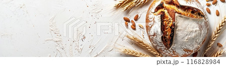 A freshly baked loaf of wheat bread sits on a white background, surrounded by wheat sprouts. 116828984