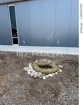 This image depicts an outdoor drainage system protected by erosion control measures. The drain is surrounded by a circular barrier made of natural fiber rolls and large river rocks. The setup ensures 116830264