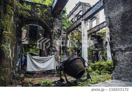 Overgrown concrete structure with cement mixer in the ruins of a building 116833172