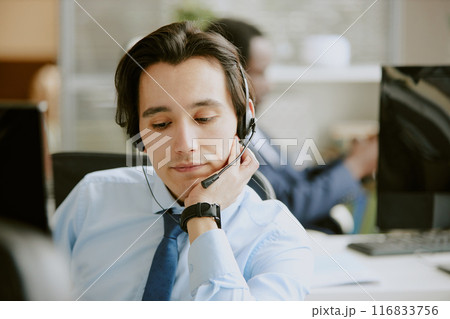 Medium close up of easy tired Caucasian male call center specialist looking at computer screen Medium close up of easy tired Caucasian male call center specialist looking at computer screen 116833756