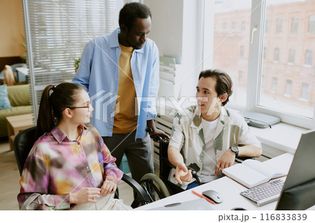 African American teamlead discussing new project with his female programmer and coworker with disability while he gesticulating African American teamlead discussing new project with his female programmer and coworker with disability while he gesticulating 116833839