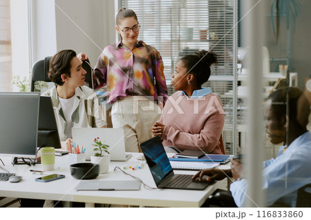 Biracial colleagues chatting in office while their african american coworker using laptop to write codes Biracial colleagues chatting in office while their african american coworker using laptop to write codes 116833860