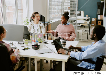 Biracial colleagues discussing next goals while sitting at white table in modern IT company office equipped with electronic devices Biracial colleagues discussing next goals while sitting at white table in modern IT company office equipped with electronic devices 116833870
