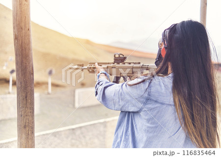 Woman empowered shooter aiming assault rifle at target. Selective Focus 116835464