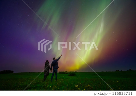 A couple marveling at the beauty of the Northern Lights under a starlit sky in a verdant field A couple marveling at the beauty of the Northern Lights under a starlit sky in a verdant field 116835711