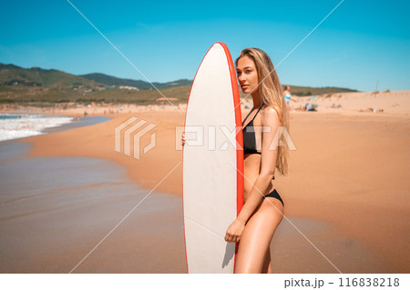 Woman surfer posing with surfboard at beach on 116838218
