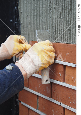 A bricklayer is seen applying mortar on a wall as part of the building construction process A bricklayer is seen applying mortar on a wall as part of the building construction process 116838976