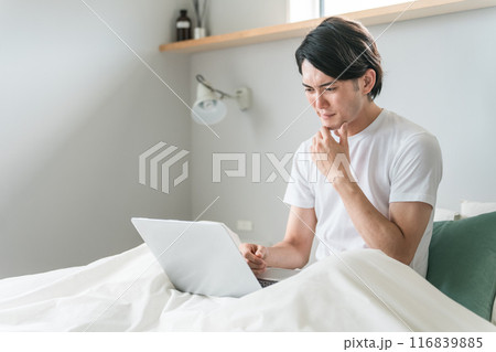 家・ホテルの寝室・ベッドルームでノートパソコンを使う若い男性（フルリモート・在宅勤務・ニュース） 116839885