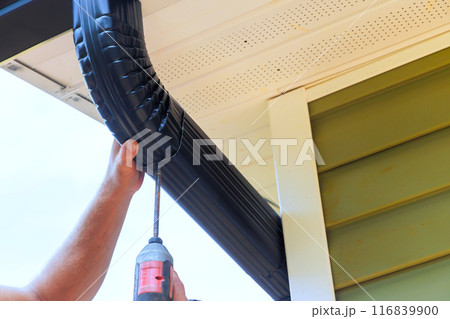 During installation of rain gutters on roofs, worker is fitting downpipe bending downspout 116839900