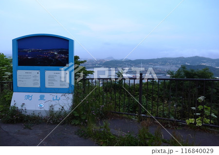 日没前の測量山展望台の案内看板と室蘭港の街並み 116840029