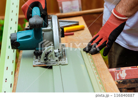 With circular hand saw, worker cuts plastic vinyl siding to required size 116840887